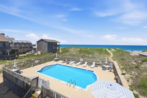 A pool area with lounge chairs, a wooden deck, and a view of the beach and ocean.