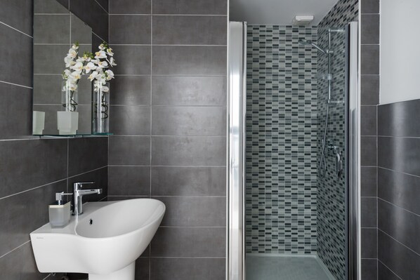 A modern bathroom with a white sink, a glass shower enclosure, and a tiled shower wall.
