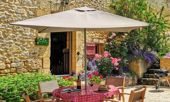 Eine Außenpatio mit einem runden Tisch, Stühlen, einem großen Sonnenschirm und einem Grill.
