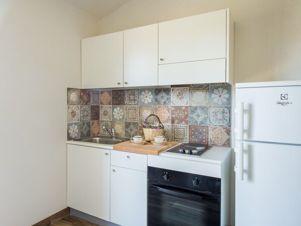 A compact kitchen with white cabinets, a tiled backsplash, a built-in oven, and a refrigerator.
