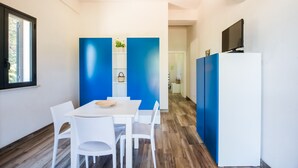A modern room with a white table and chairs, a TV on a white cabinet, and blue accent walls. - L Ulivo Blu - One-bed 2 With Seaview Balcony -loc (Castellammare del Golfo)