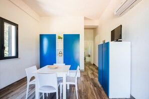 Une pièce moderne avec une table et des chaises blanches, un téléviseur posé sur un meuble blanc et des murs d’un bleu vif.