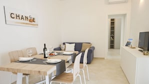 A modern dining area with a wooden table set for four, a grey sofa, and a white TV stand with a picture frame. - Blue Sea - Villa Scirocco 33 - Locz (Ostuni)