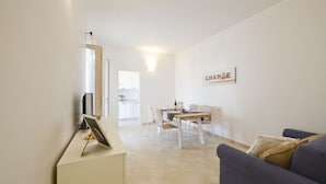Una sala de estar con un sofá azul, una mesa de comedor con sillas y una cocina al fondo.