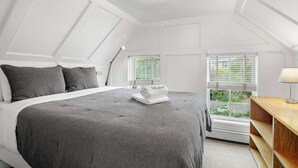 A bedroom with a large bed, a desk, and a window with blinds.
