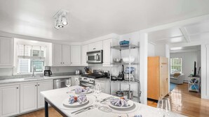 A modern kitchen with white cabinetry, a central island with a marble countertop, and a dining area set for six.