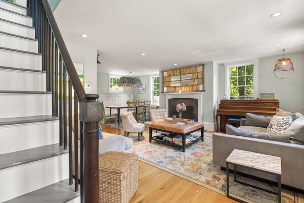 A spacious living room with a fireplace, a piano, and a staircase.