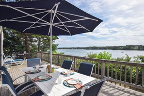 A deck with a table set for dining, overlooking a lake.