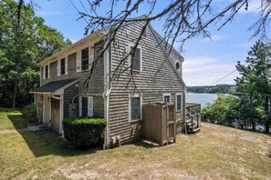 A two-story wooden house with a dock extending into a lake, surrounded by trees.