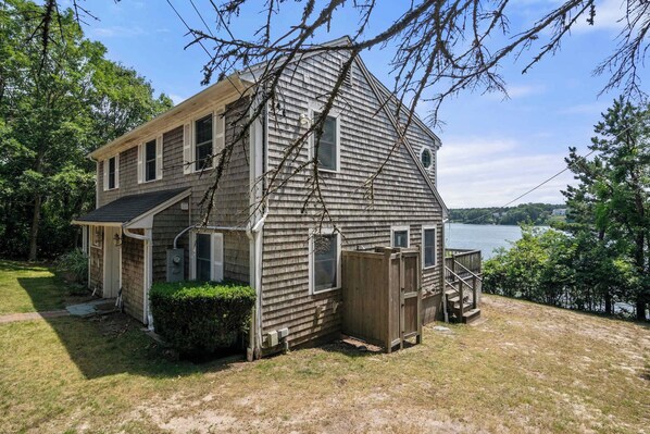 A two-story wooden house with a dock extending into a lake, surrounded by trees.
