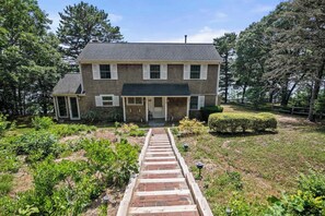 A two-story house with a front porch, a brick pathway leading to the entrance, and a well-maintained garden with various plants.