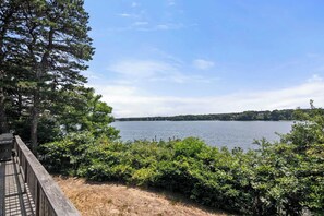 A wooden deck overlooking a lake with dense greenery and a distant shoreline. - Waterfront on Follins Pond! (Dennis)