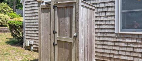A wooden shed with a sliding door, positioned next to a house with siding and a window.