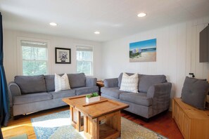 A living room with two grey sofas, a wooden coffee table, and a painting of a beach scene.