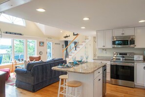 A spacious living area with a dark blue sofa, a wooden staircase, and a kitchen with stainless steel appliances. - Waterfront on Follins Pond! (Dennis)