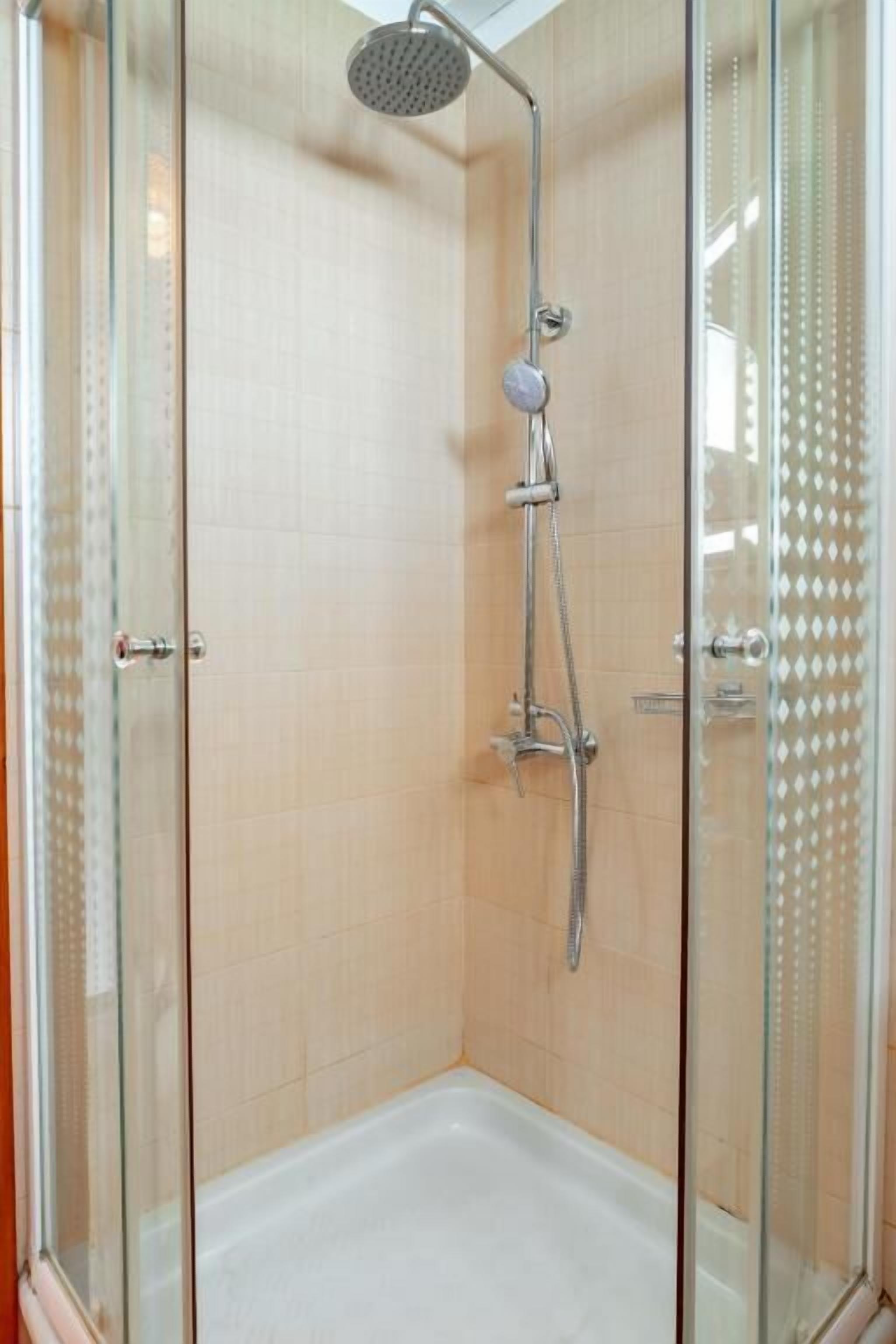 A glass-enclosed shower stall with a handheld showerhead and a wall-mounted faucet.
