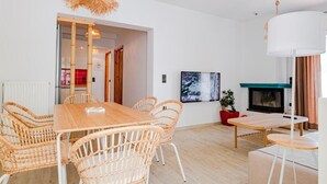 Una sala de estar moderna con una mesa de comedor de madera, sillas de mimbre, una chimenea y un cuadro grande en la pared.