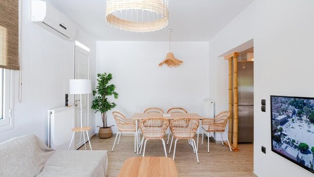 Una sala moderna con sofá, mesa de comedor, sillas, lámpara colgante, planta en maceta y televisor en la pared.