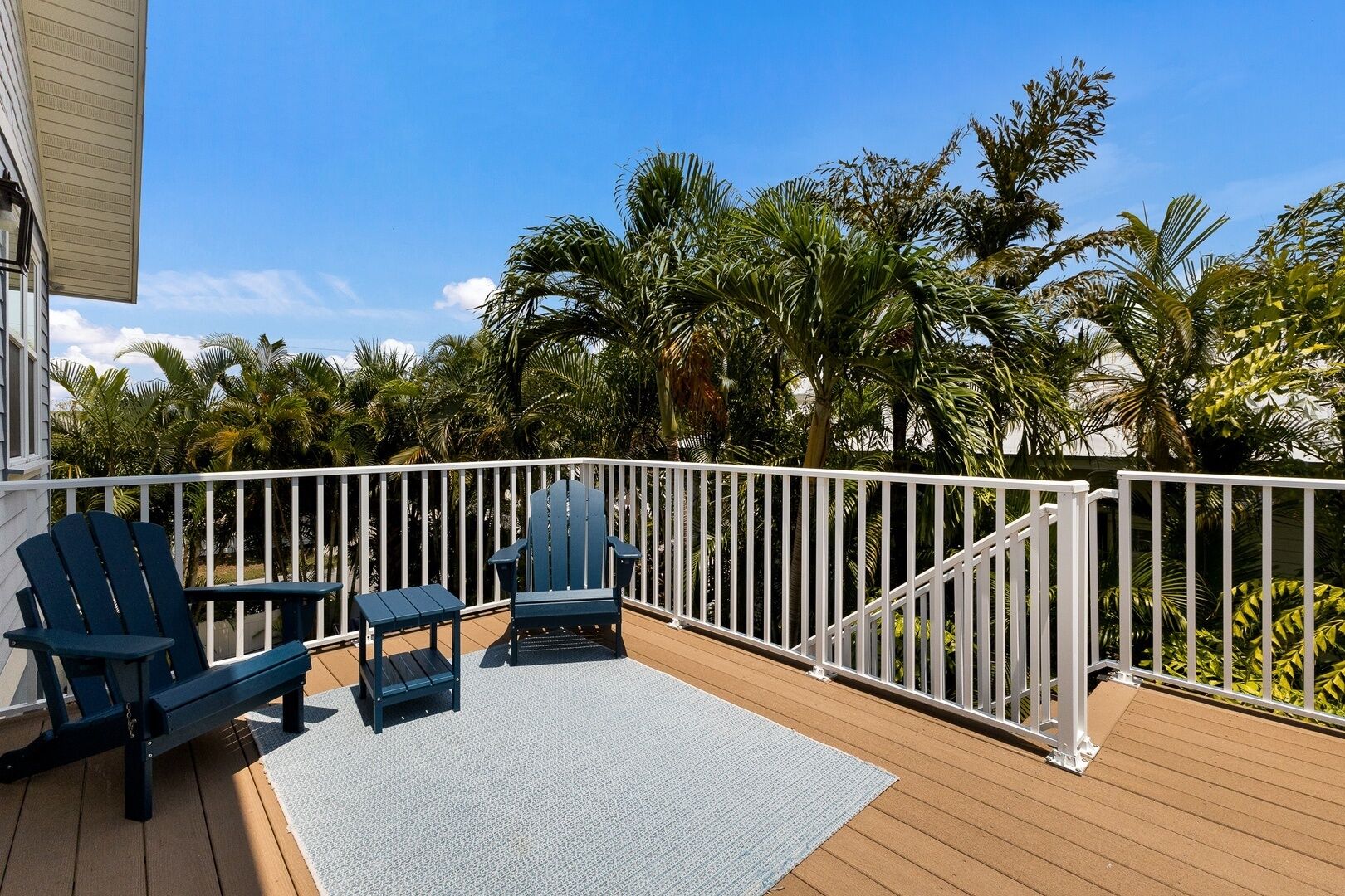 Una terraza de madera con baranda blanca, dos sillas Adirondack y una pequeña mesa.
