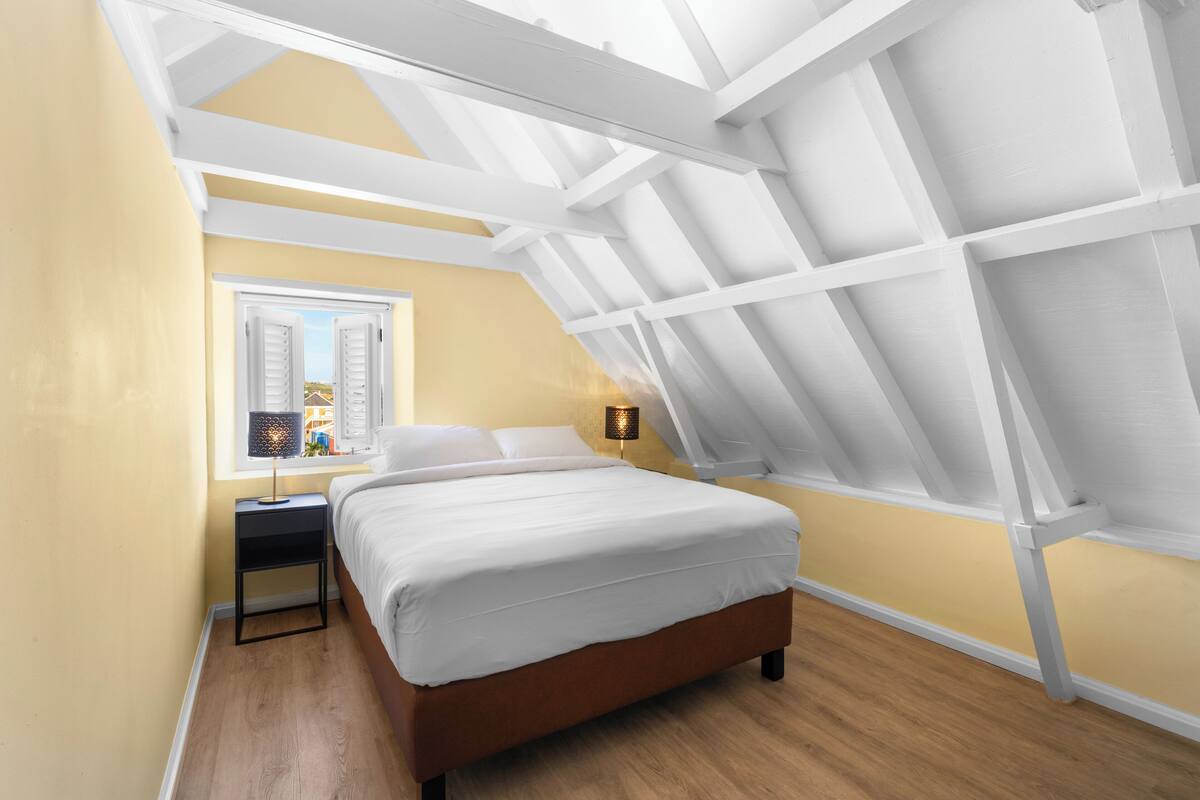 A bedroom with a skylight, a bed, a nightstand, and a lamp.