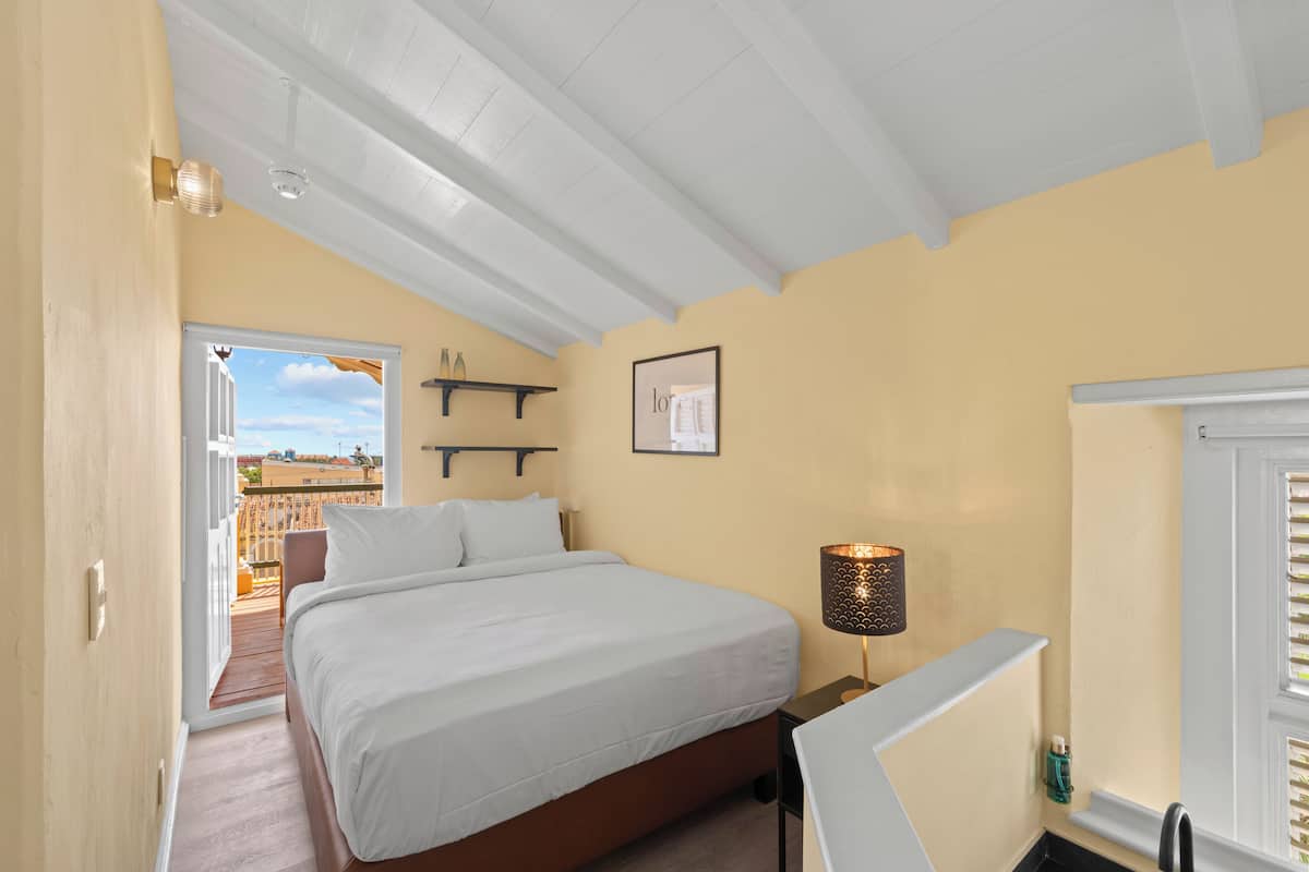 A bedroom with a bed, bedside table, lamp, and a window with blinds.