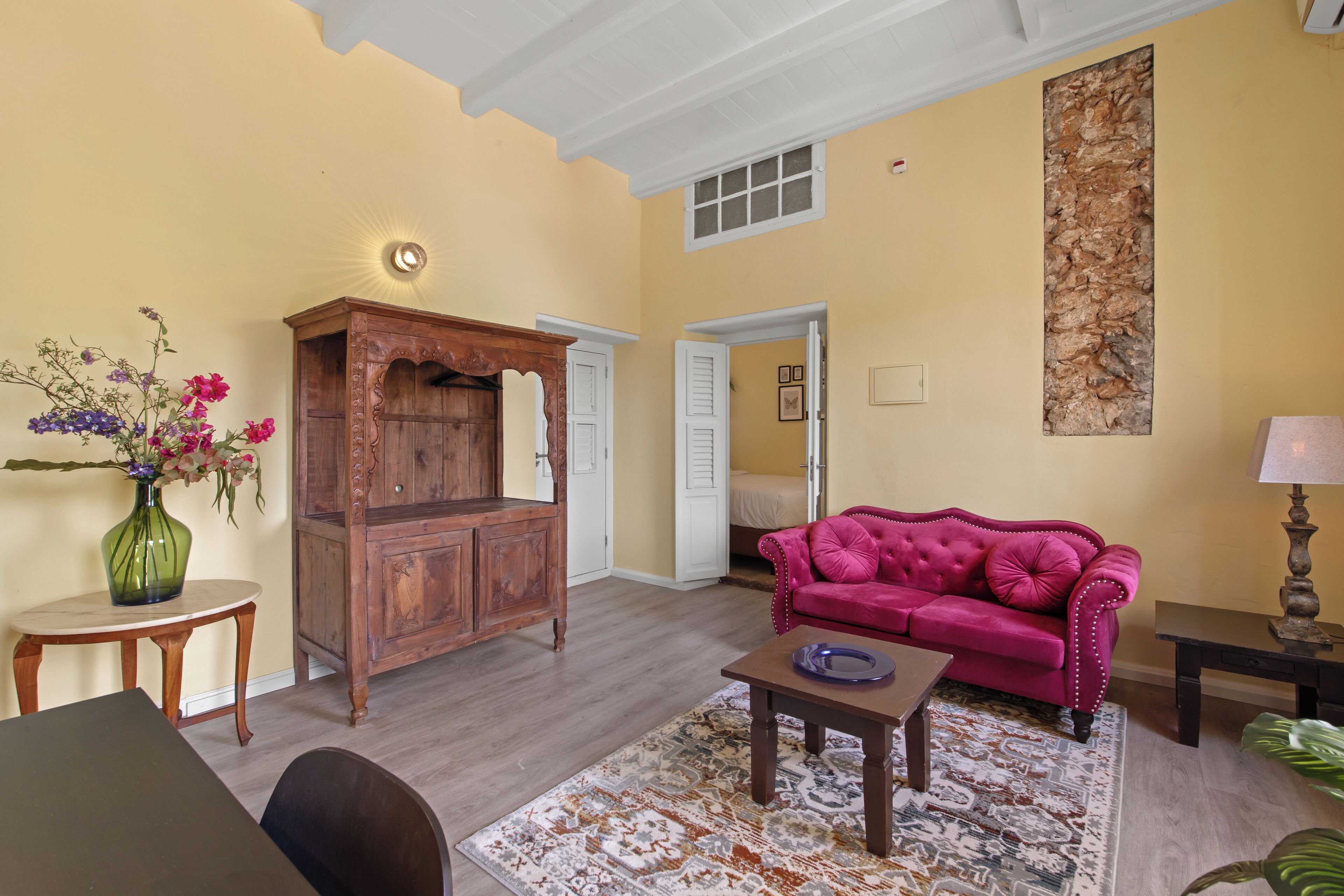 A living room with a wooden cabinet, a pink sofa, a small table, and a vase with flowers.