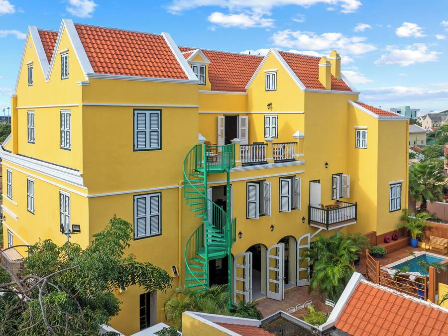 A yellow building with a red-tiled roof, a green spiral staircase, and a pool area.