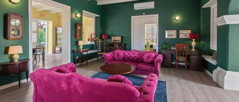 Een ruime woonkamer met een grote roze bank, een salontafel, en een eethoek met een houten tafel en stoelen.