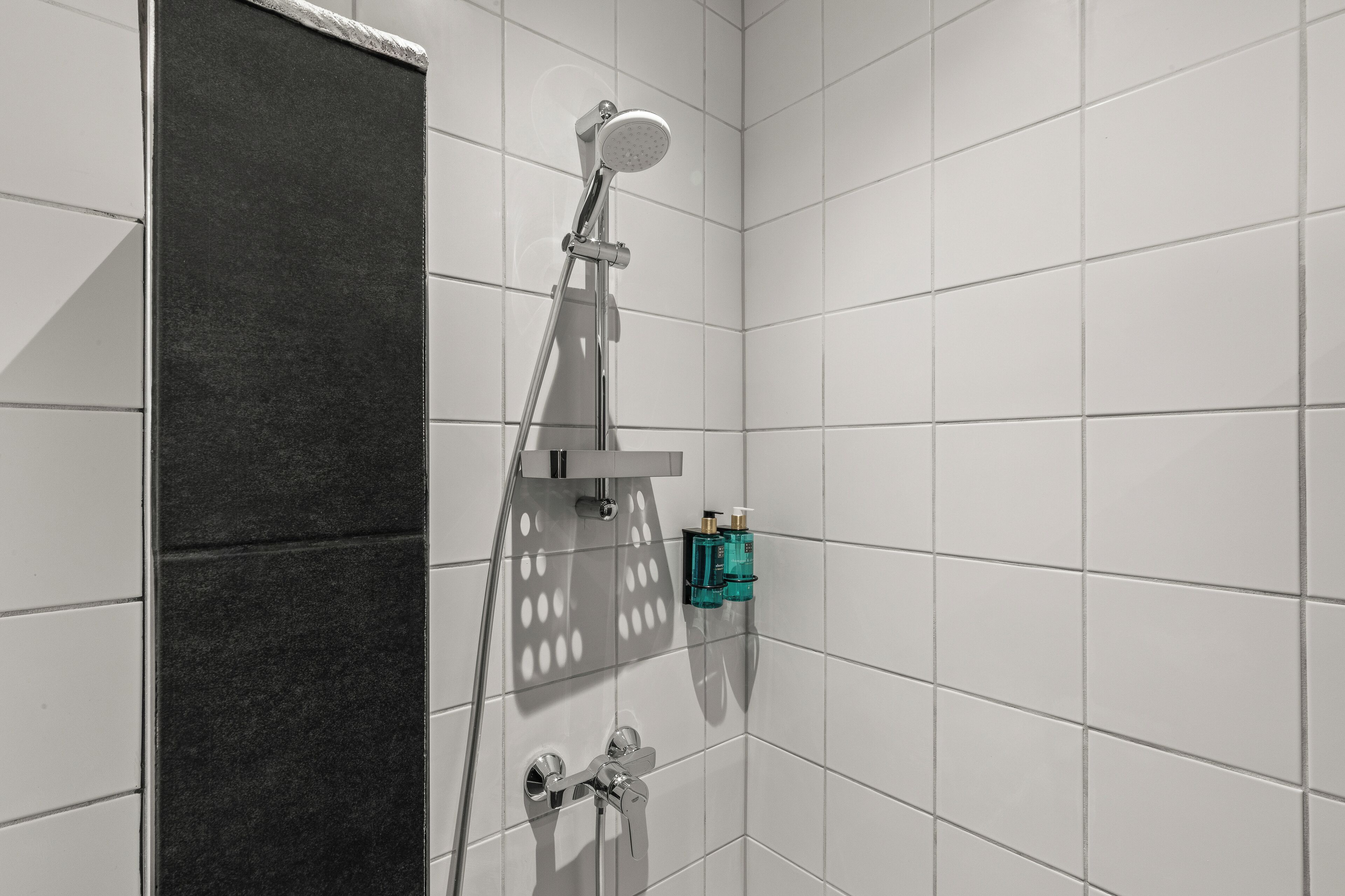 Une salle de bain moderne avec des carreaux blancs, une douche équipée d’un pommeau de douche à main et un porte-serviettes.