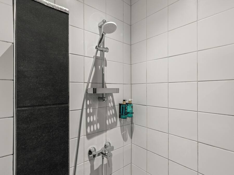 A modern bathroom with white tiles, a shower with a handheld showerhead, and a towel rack.
