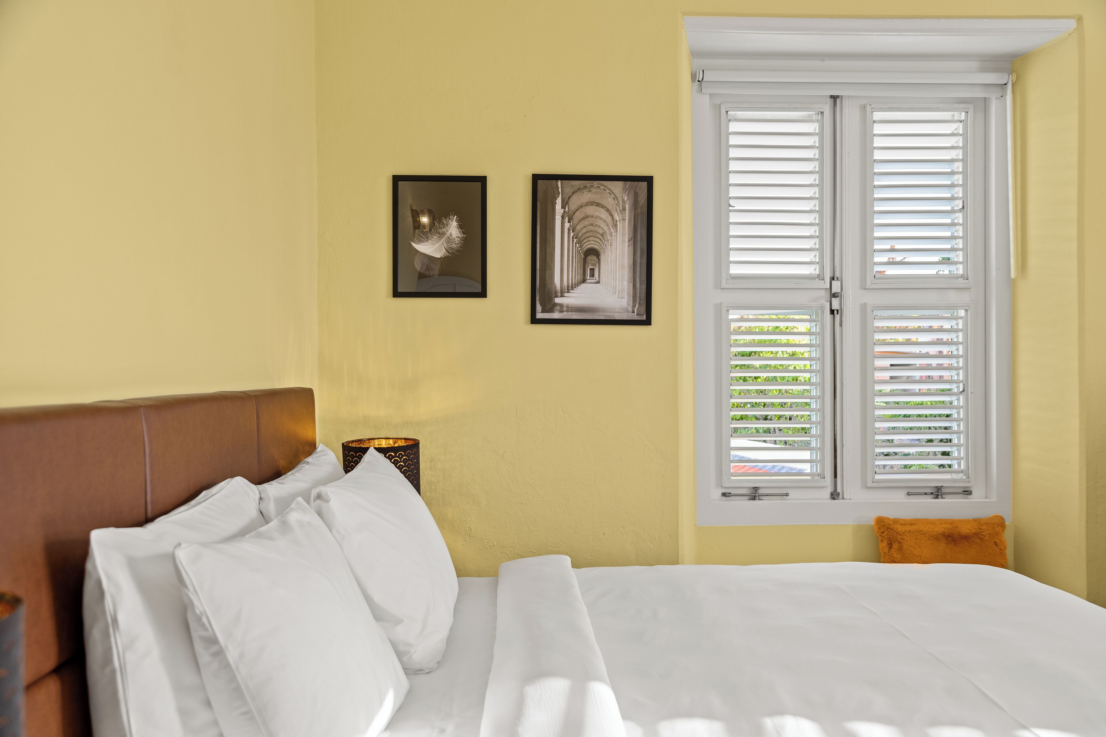 Ein ordentlich bezogenes Bett mit weißer Bettwäsche, einem hölzernen Kopfteil und einem Fenster mit weißen Fensterläden.