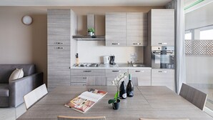 A modern kitchen with grey cabinetry, a dining table with a magazine, two wine bottles, and a potted plant. - Residenza Miralago - 24 Clodia - Locazione BK (Desenzano del Garda)
