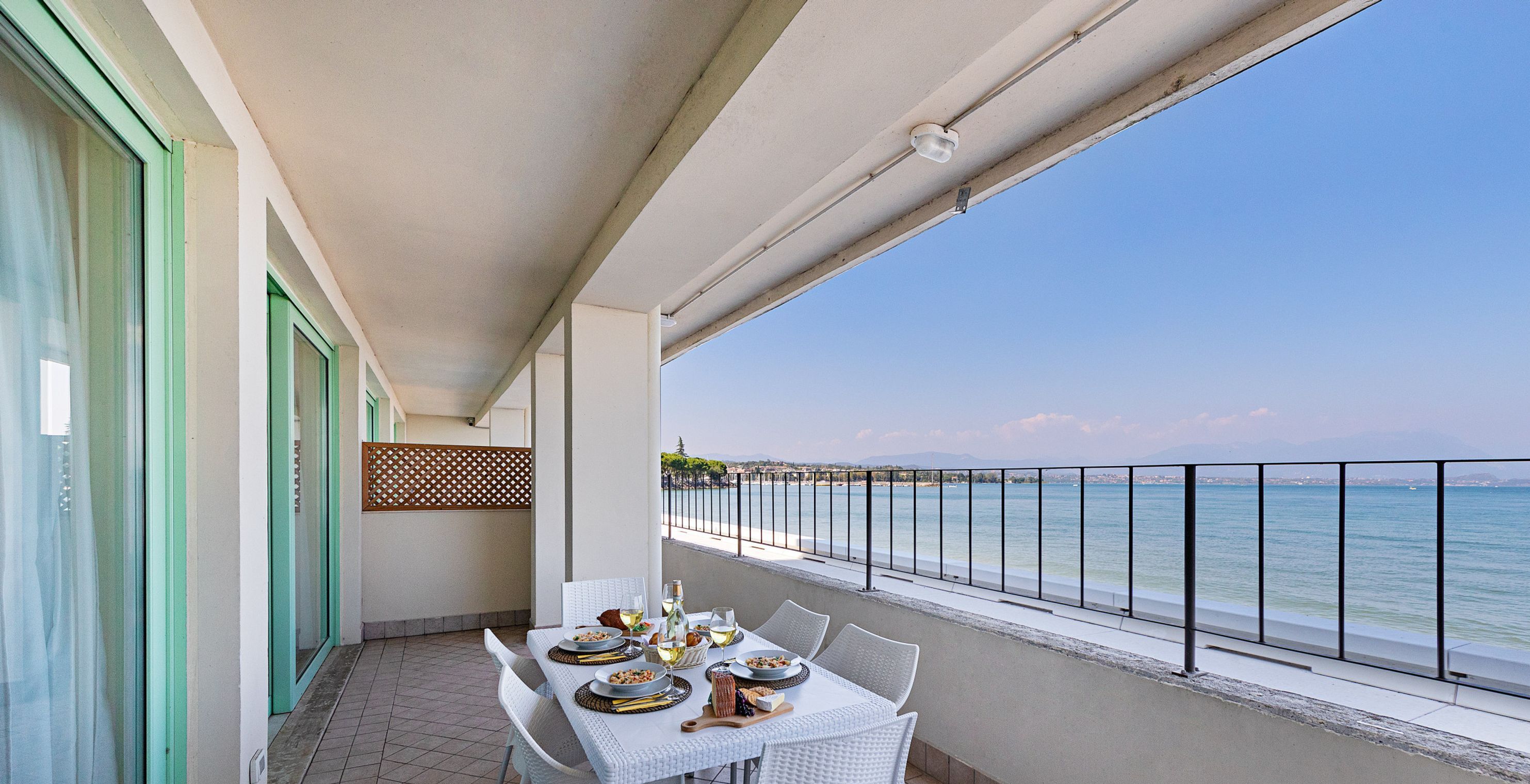 A balcony with a table set for dining, overlooking a body of water and a distant shoreline.
