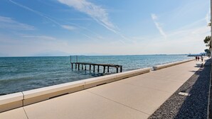 A waterfront promenade with a wooden pier extending into the water, a clear sky, and distant mountains. - Residenza Miralago - 24 Clodia - Locazione BK (Desenzano del Garda)