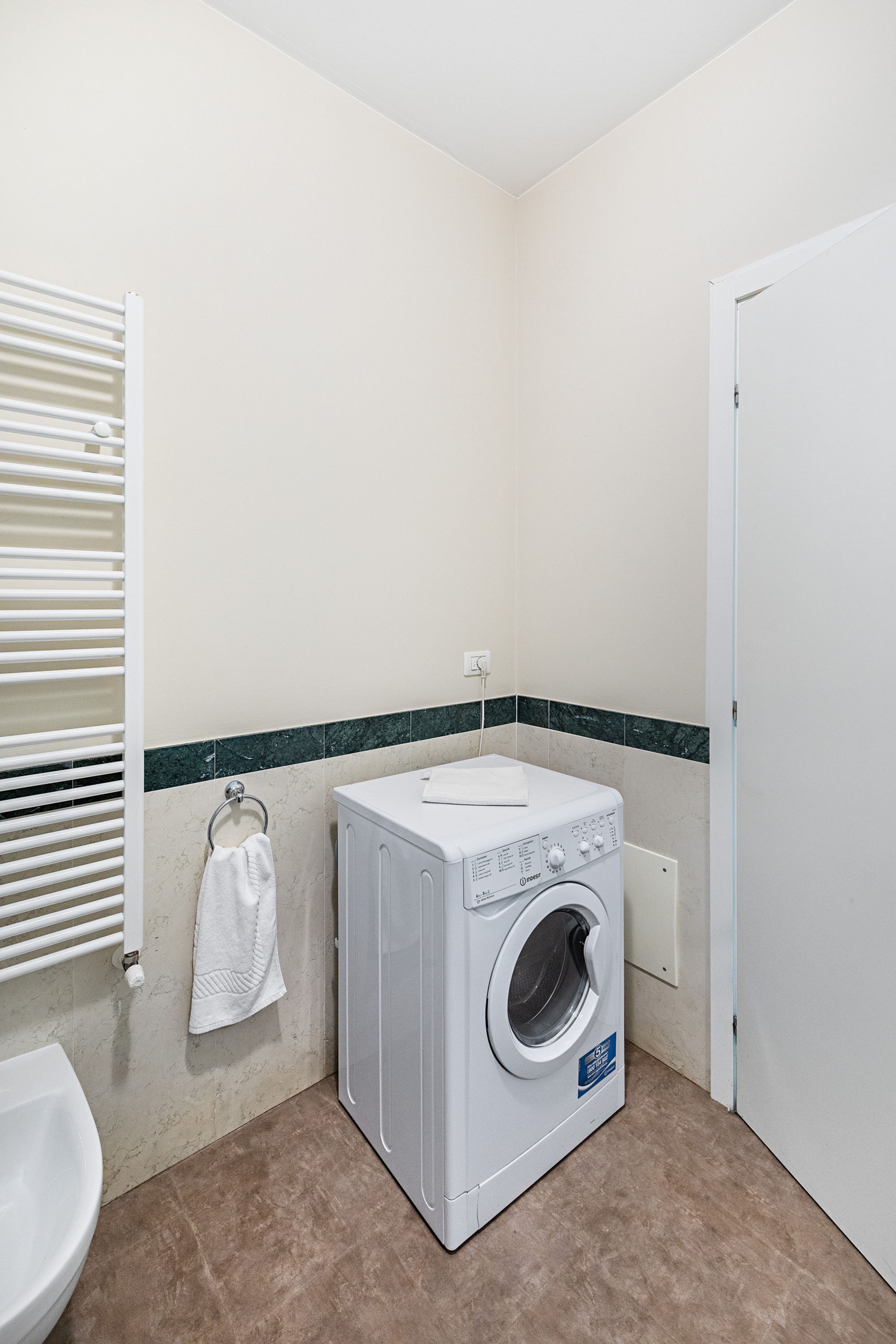 Ein kleiner Waschraum mit einer Waschmaschine, einem Handtuchhalter und einer Toilette.