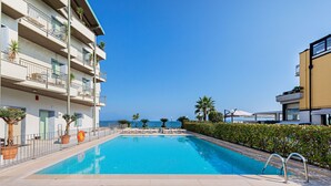 A swimming pool with a clear view of the sea, surrounded by a multi-story building with balconies and potted plants. - Residenza Miralago - 24 Clodia - Locazione BK (Desenzano del Garda)