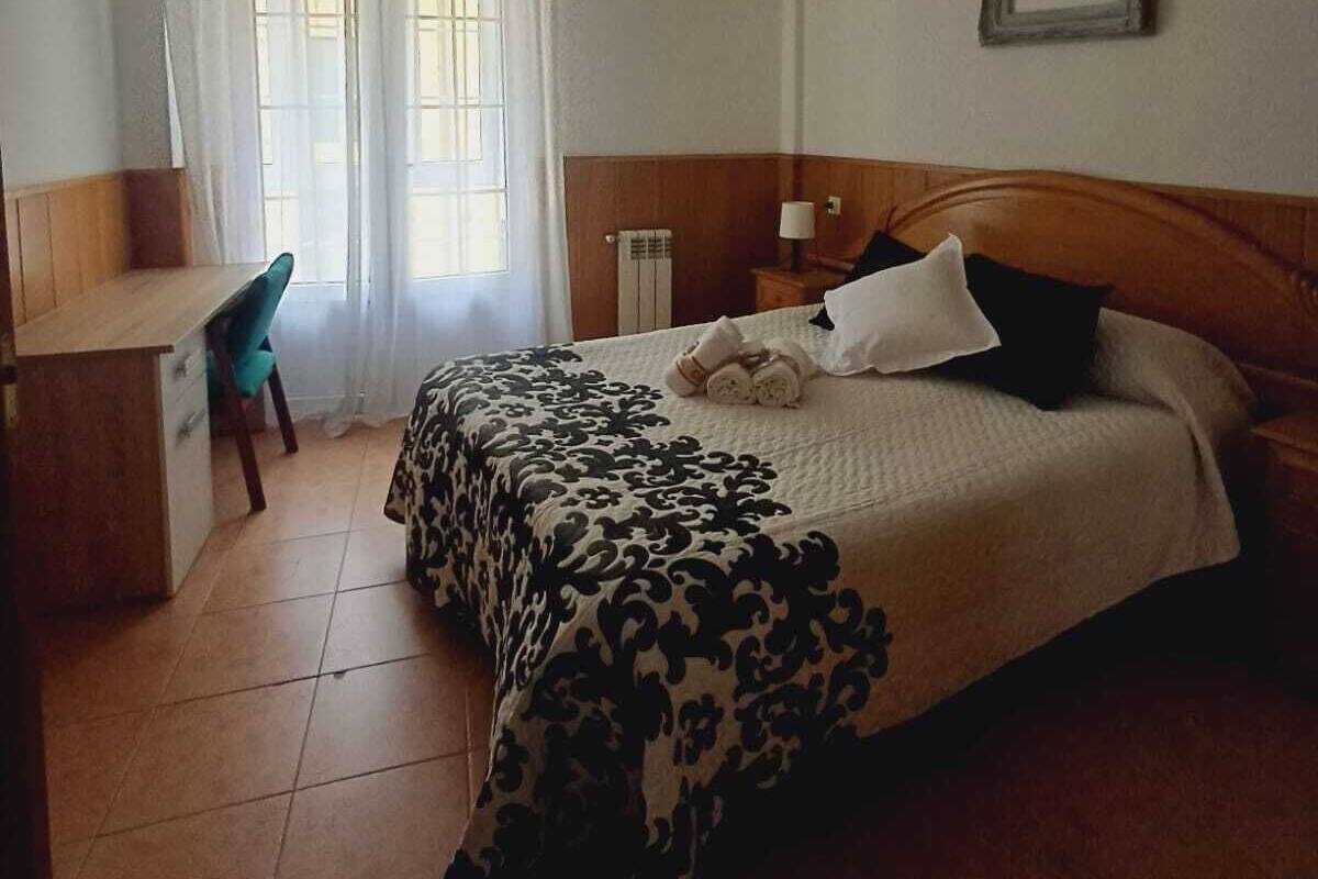 A bedroom with a bed, a desk, a chair, and a window with curtains.