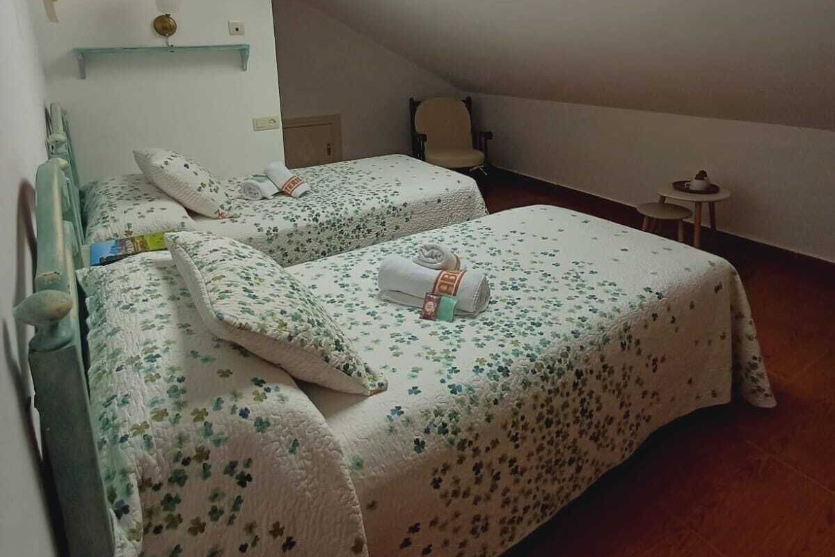A small, cozy room with a sloped ceiling and skylight, featuring two beds with floral bedding and a small table with a cup and saucer.