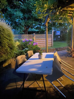 An outdoor patio with a table and chairs, surrounded by a wooden fence and greenery. - Charming 1-bedroom Annex,hot tub in stunning mendip retreat, near BristolAirport (Churchill)