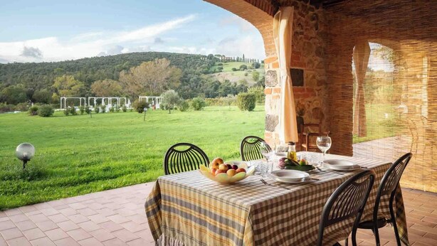 Un área de comedor al aire libre con una mesa dispuesta para dos, con vistas a un paisaje verde exuberante y una colina en la distancia.