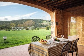 Un área de comedor al aire libre con una mesa dispuesta para dos, con vistas a un paisaje verde exuberante y una colina en la distancia.