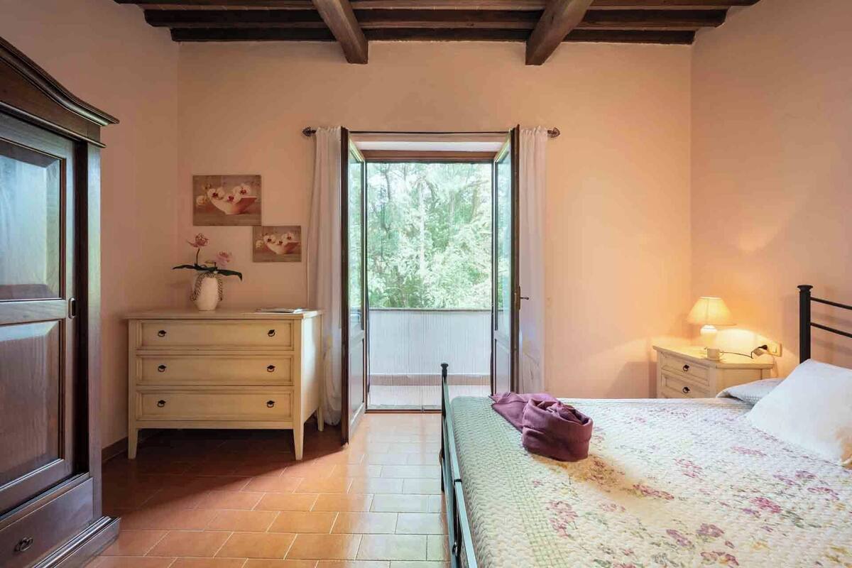 A bedroom with a bed, a nightstand, a dresser, and a window with a view of trees.