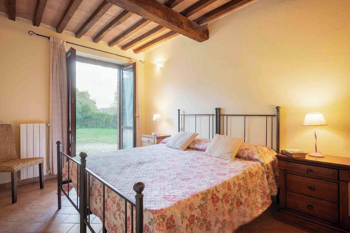 A bedroom with a bed, bedside tables, a chair, and a view of the outdoors.