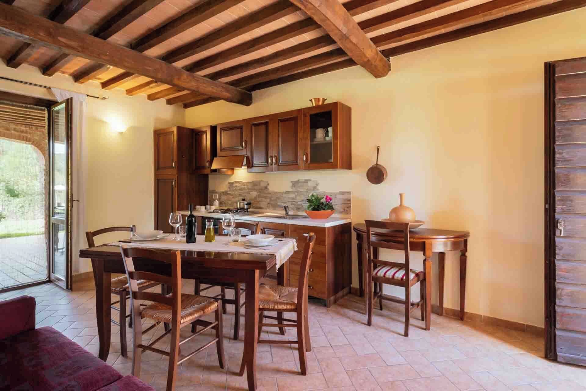 A rustic kitchen with wooden cabinets, a central island, and a dining area with chairs and a table.