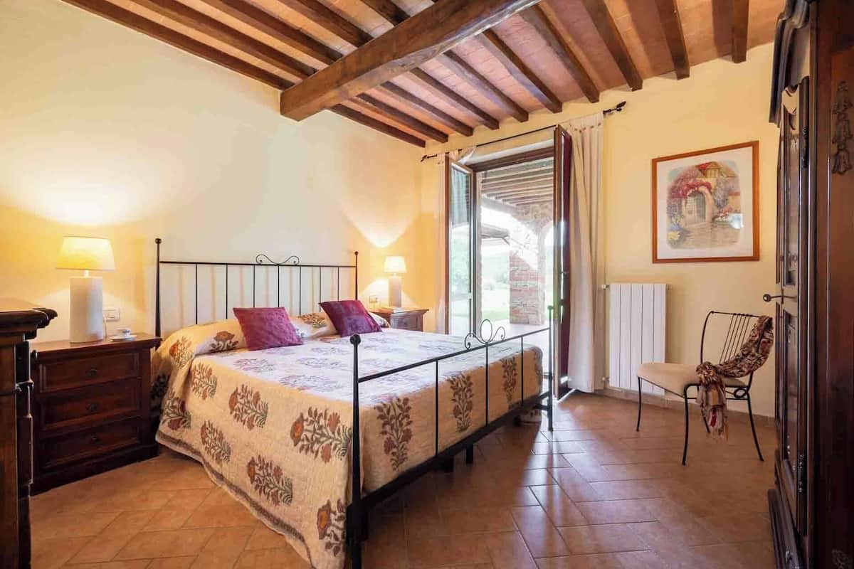 A bedroom with a bed, bedside lamps, a chair, and a window with a view.