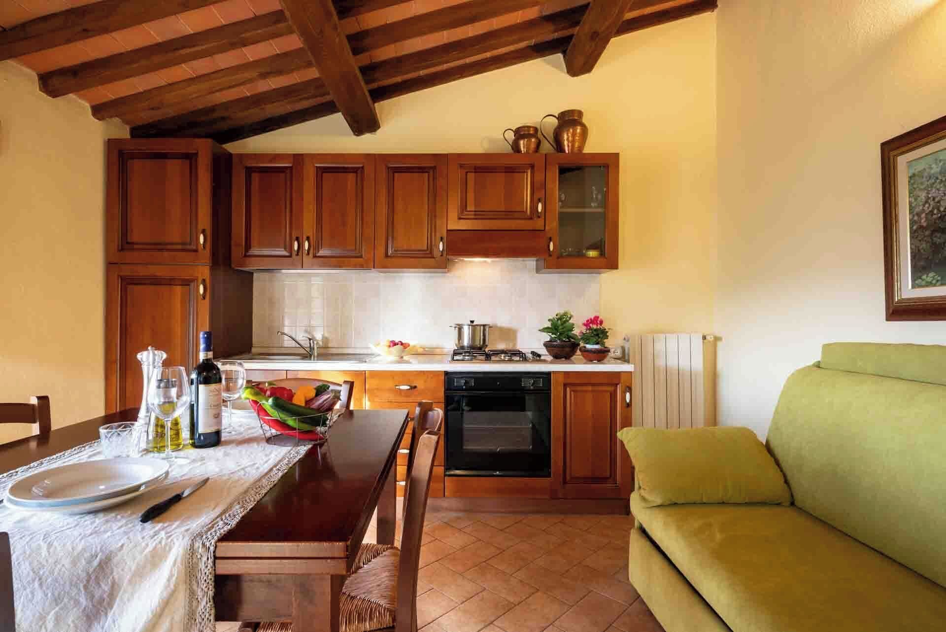 Eine gemütliche Küche mit Holzausbau, einem Esstisch gedeckt mit Geschirr und Besteck, einem grünen Sofa und einem Fliesenboden.