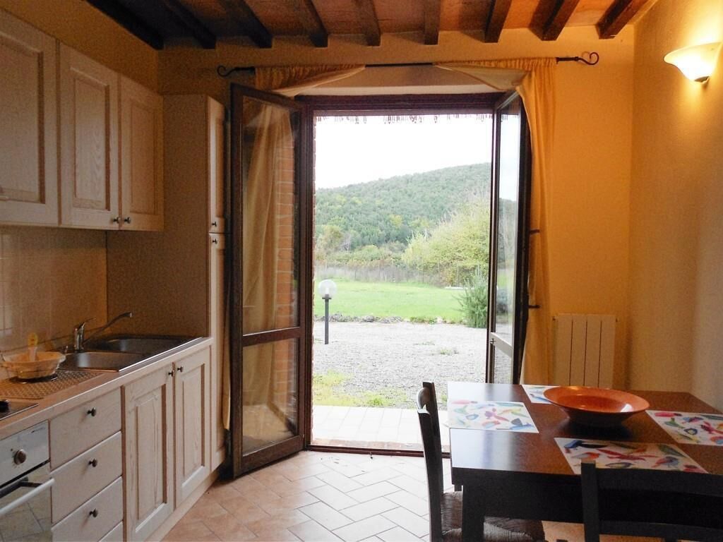 Una cocina con un ventanal grande, una mesa de comedor con un cuenco, y vista a un paisaje verde.