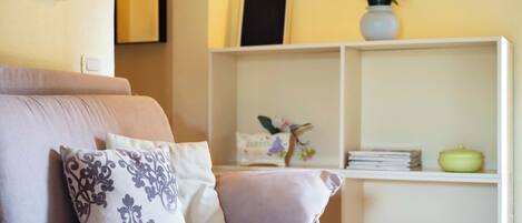 A cozy living room with a sofa, pillows, a bookshelf, and decorative items.