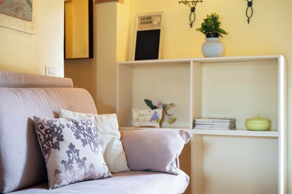 Una sala de estar acogedora con un sofá, cojines, una estantería y objetos decorativos.