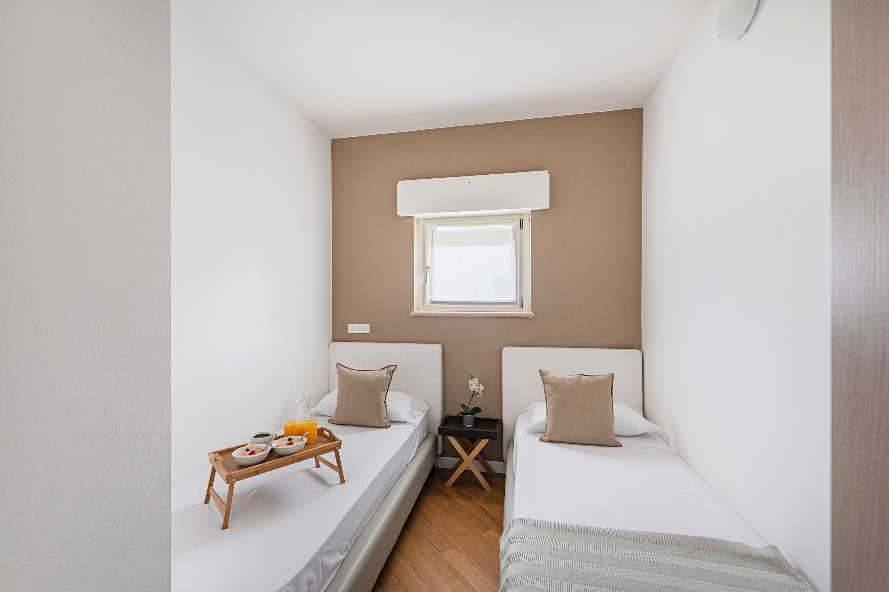 A small, modern room with two single beds, a small table with breakfast, a window, and a ceiling fan.